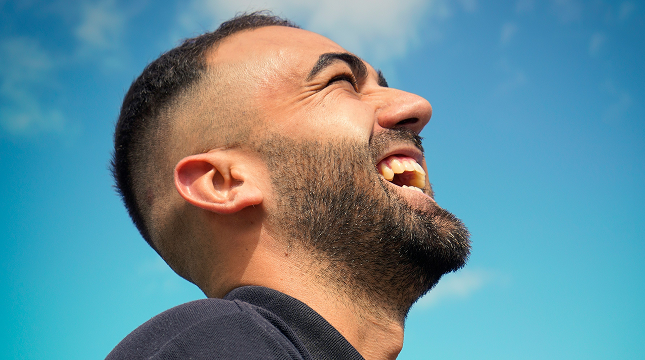 Man laughing outdoors under a clear blue sky, free from glasses